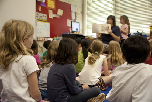 Children in a classroom listening to a book being read by the teacher
